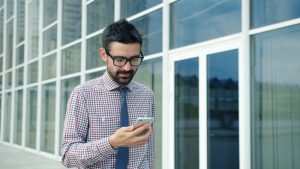 Man in glasses looking at his phone outside building